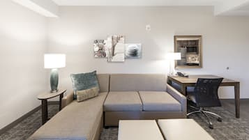 A hotel room with a sofa, two side tables, a desk, a chair, and artwork on the wall.