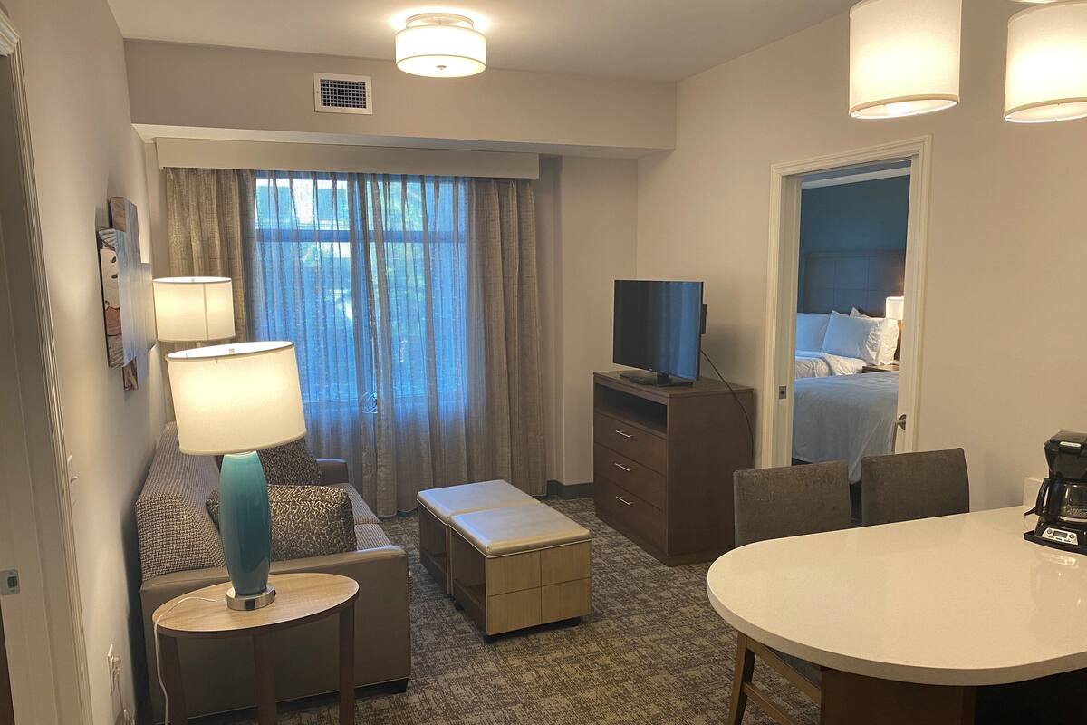 A hotel room with a bed, a TV, a desk, a chair, a lamp, and a coffee maker.