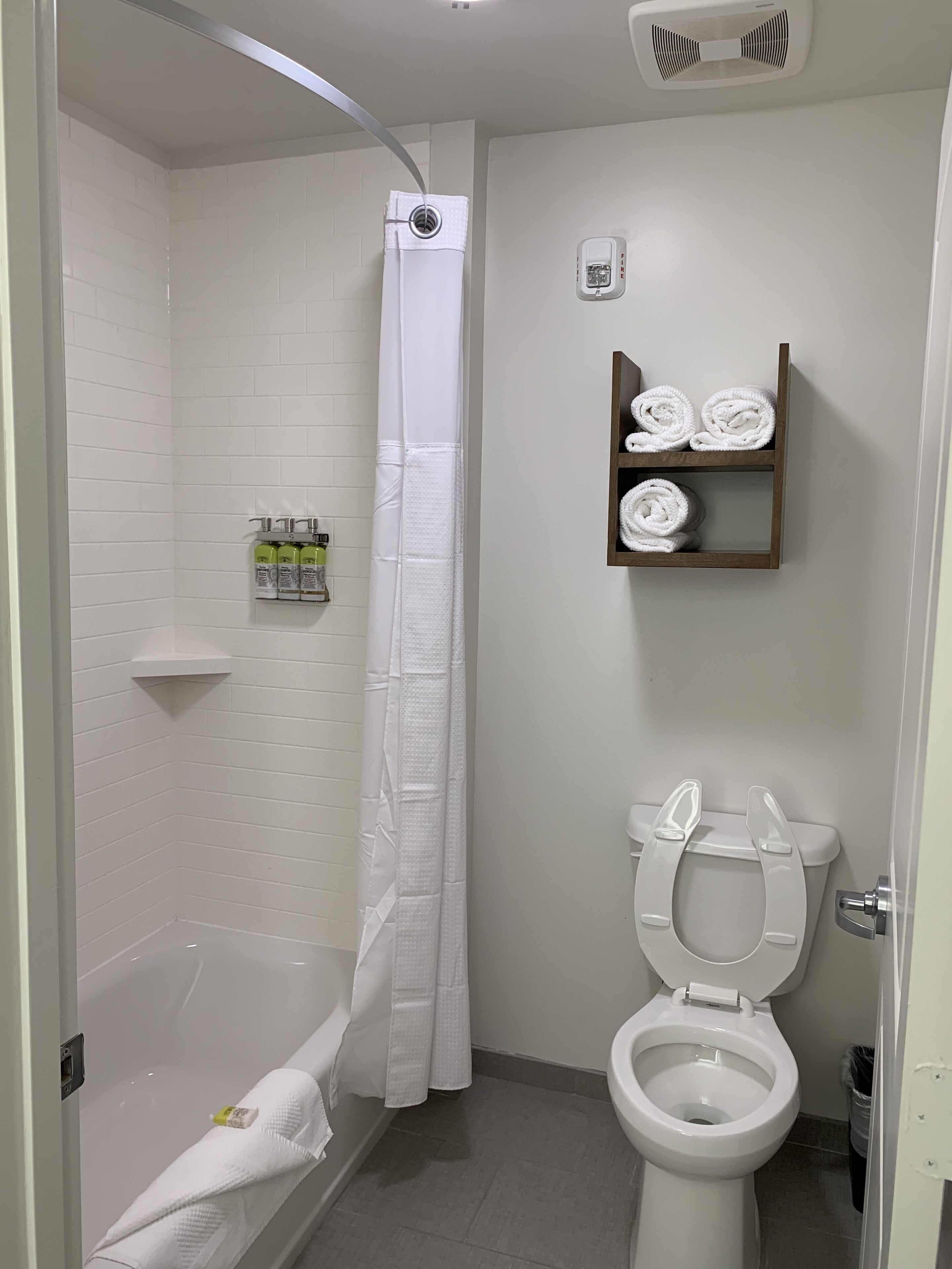A bathroom with a shower, toilet, and a shelf with towels.