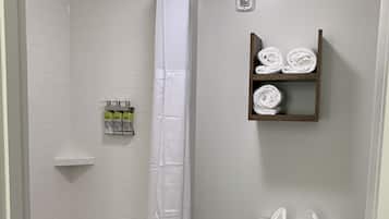 Un baño con ducha, inodoro y un estante con toallas.