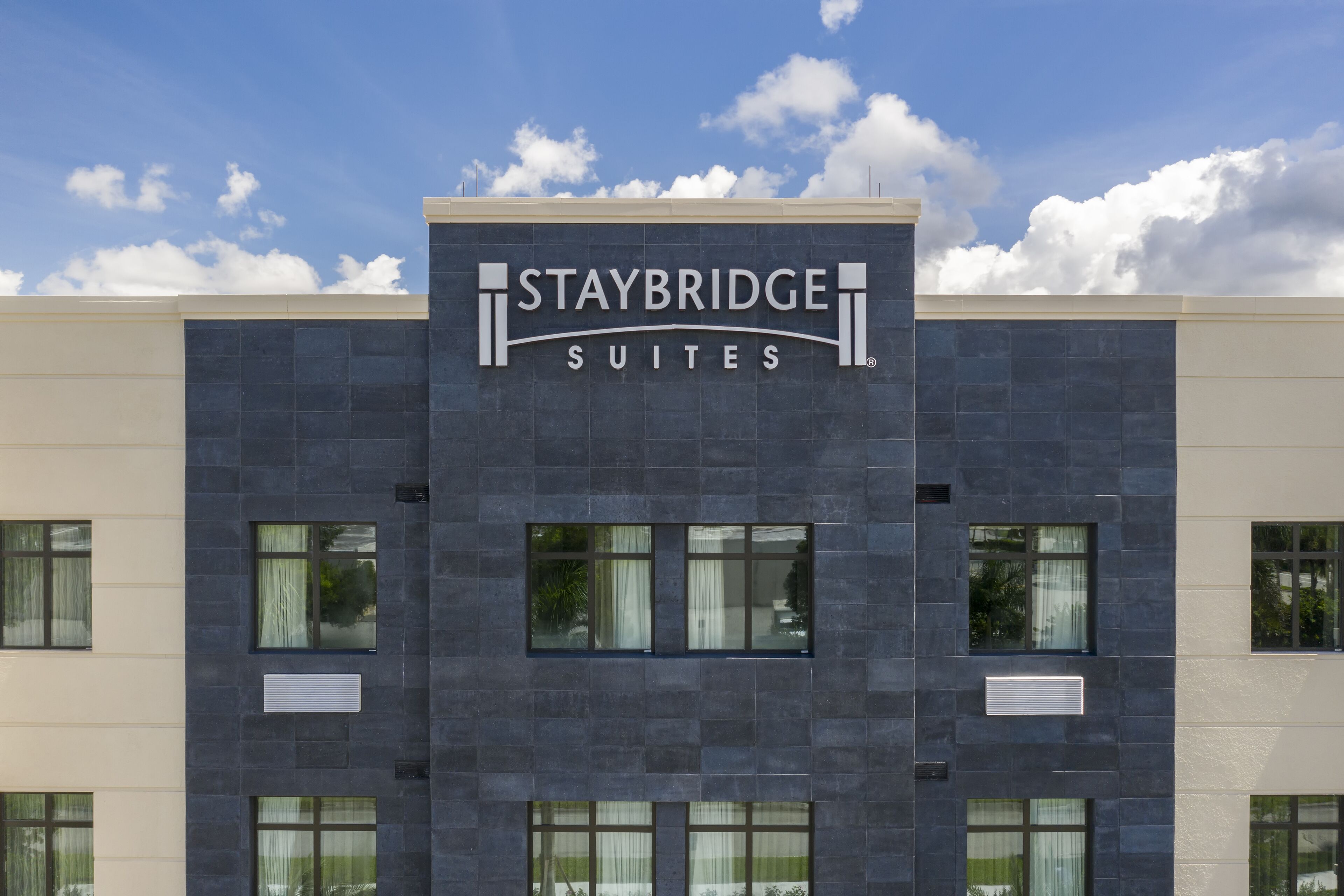 Ein Staybridge Suites Gebäude mit moderner Fassade, großen Fenstern und blauem Himmel.