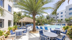 A poolside area with lounge chairs, a palm tree, and a thatched-roof structure. - Staybridge Suites Naples – Marco Island by IHG (Naples)
