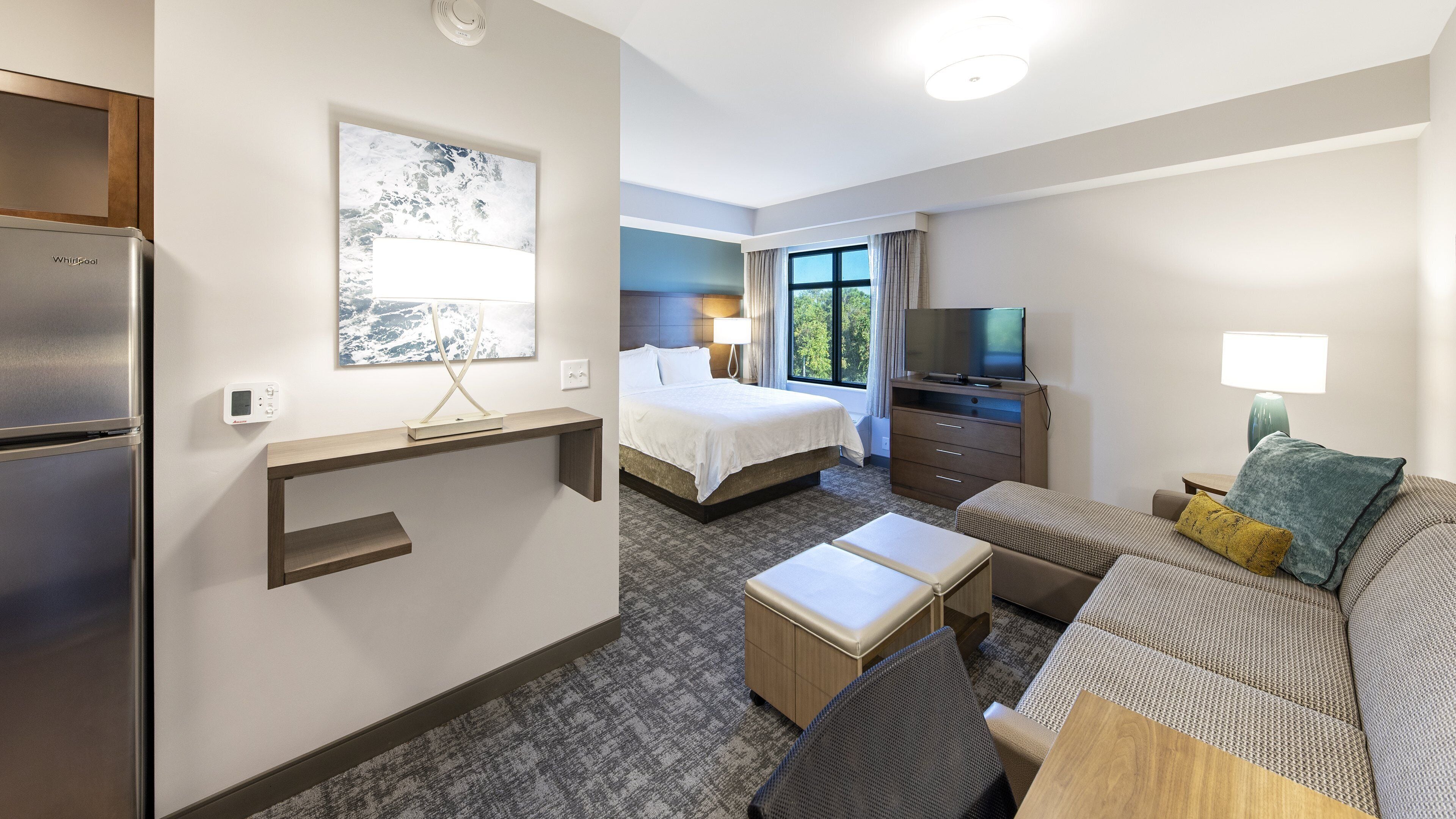 A hotel room with a bed, a sofa, a TV, a refrigerator, a desk, and a window with a view.