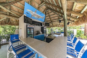 A restaurant with a thatched roof, blue chairs, and a counter with a menu.