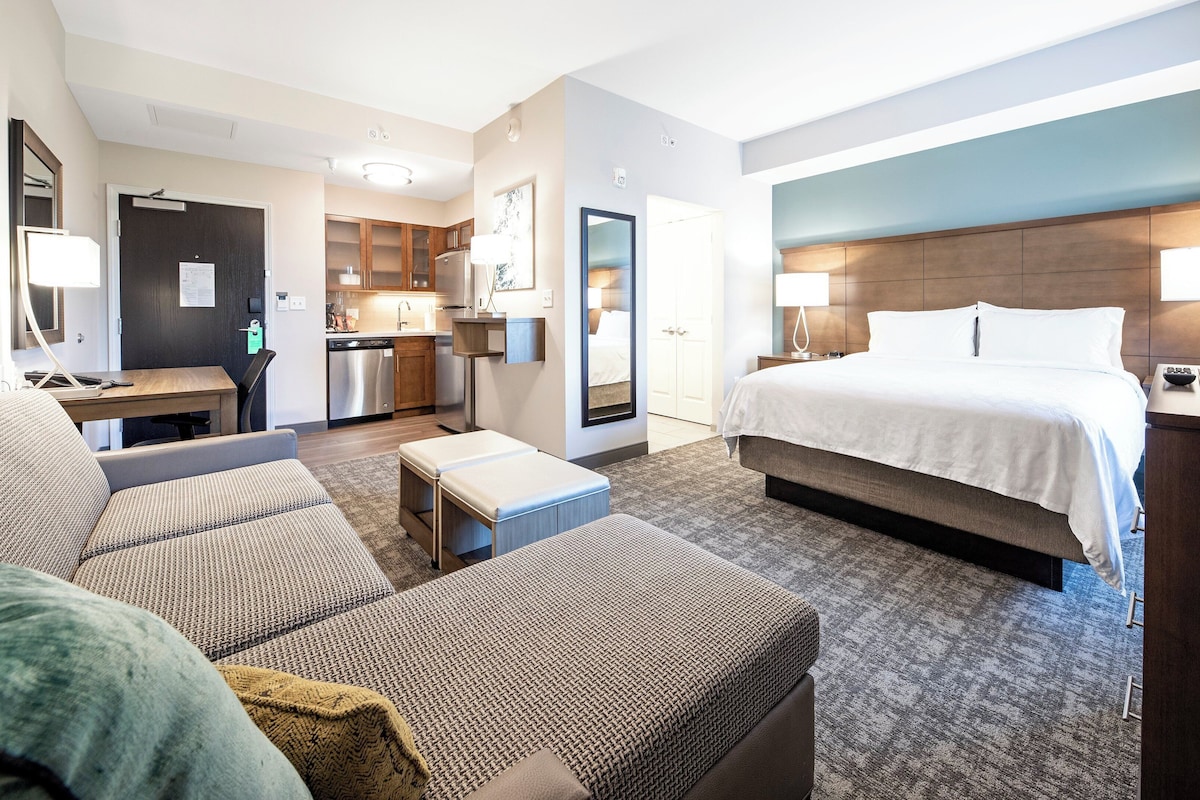 A hotel room with a bed, a sofa, a desk, and a kitchenette.