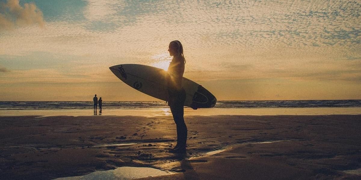 A person holding a surfboard on a beach at sunset.