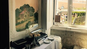 A dining area with a view of a courtyard, a painting on the wall, and a buffet setup with plates and a bottle. - LUXa Charmhouse Hotel (Sintra)