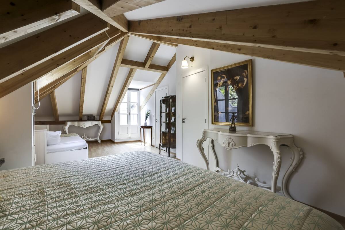 Une chambre avec un plafond en pente, un lit recouvert d’une courtepointe à motifs, une commode blanche, une chaise blanche, une armoire blanche, une table de chevet blanche, une table blanche, une lampe blanche, une console blanche, une chaise blanche, un lampadaire blanc, un mur blanc, un plafond blanc, une porte blanche, une fenêtre blanche, un ventilateur de plafond blanc, une horloge murale blanche, un cadre photo blanc, une photo blanche, une photo blanche accrochée au mur, une photo blanche accrochée au mur, une photo blanche accrochée au mur, une photo blanche accrochée au mur, une photo blanche accrochée au mur, une photo blanche accrochée au mur, une photo blanche accrochée au mur, une photo blanche accrochée au mur, une photo blanche accrochée au mur, une photo blanche accrochée au mur, une photo blanche accrochée au mur, une photo blanche accrochée au mur, une photo blanche accrochée au mur, une photo blanche.