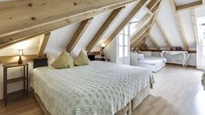 A bedroom with a sloped ceiling, a bed with a patterned bedspread, bedside tables, and a nightstand with a lamp. - LUXa Charmhouse Hotel (Sintra)