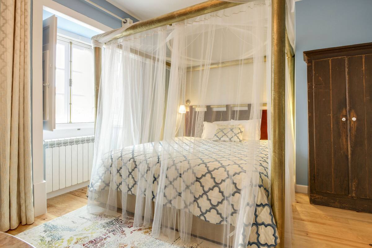 Un lit à baldaquin à quatre poteaux, agrémenté d’une couvre-lit à motifs, d’une table de chevet et d’une petite table de nuit.