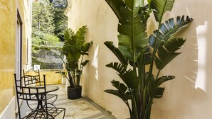 A small outdoor patio with a metal table and chairs, surrounded by large potted plants. - LUXa Charmhouse Hotel (Sintra)