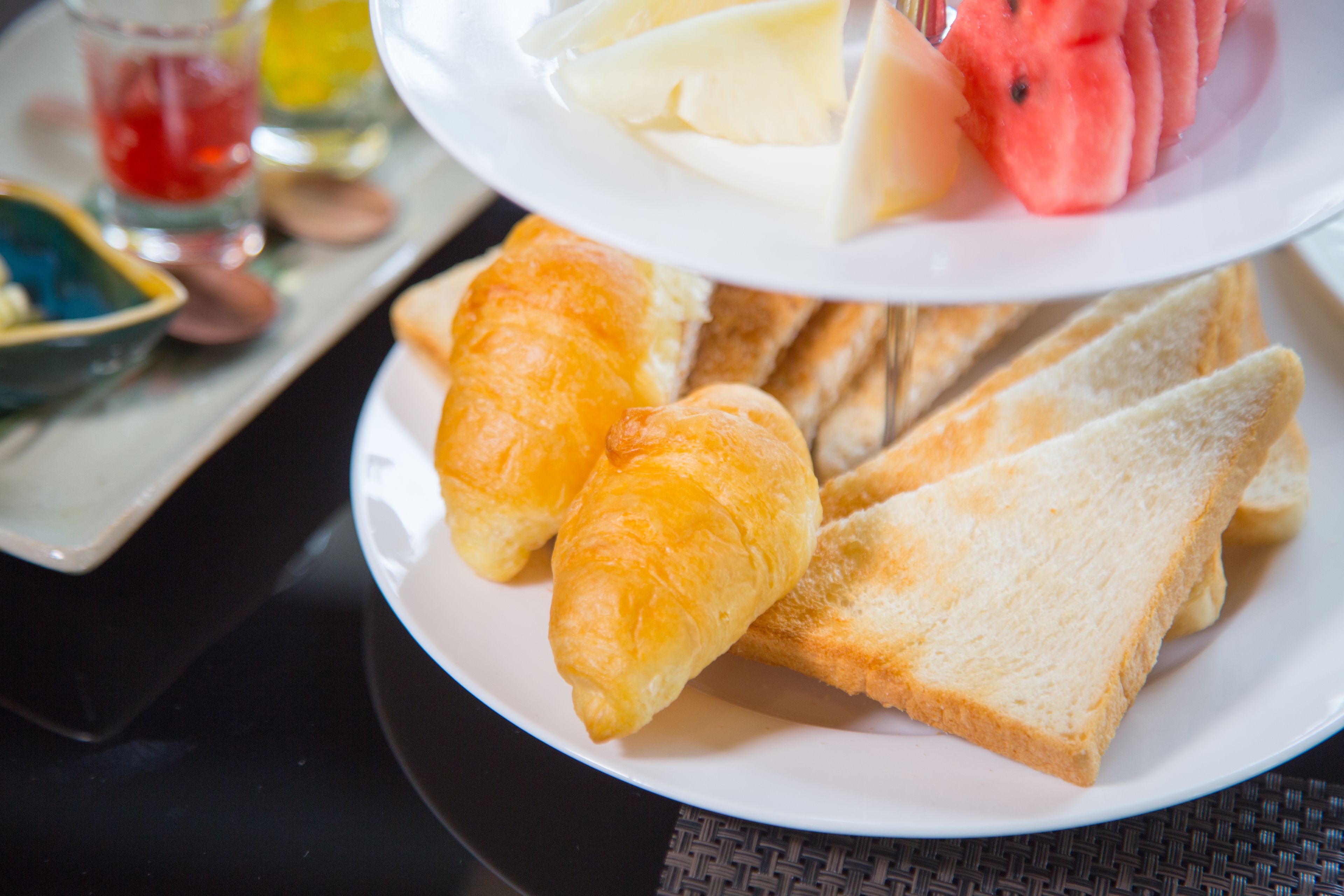 A plate with croissants, slices of bread, and watermelon on a table.