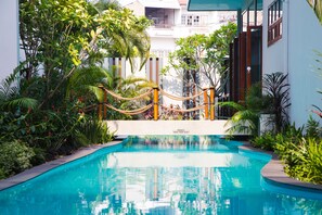 A swimming pool surrounded by lush greenery and a rope barrier. - Nai Ya Hotel (Chiang Rai)