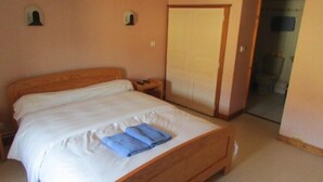 A single bed with white bedding and a blue towel, a wooden headboard, a nightstand with a phone, and a door leading to a bathroom. - Rod & Sève (Propières)