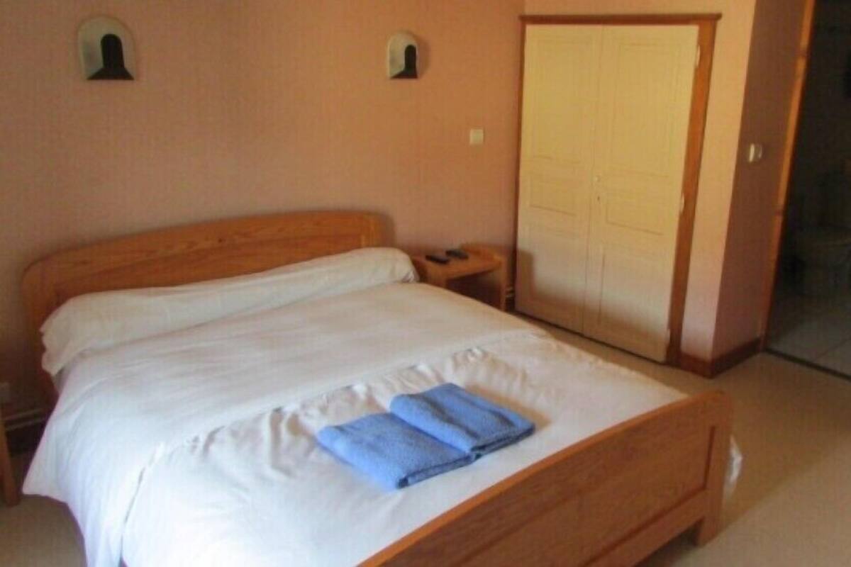 A single bed with white bedding and a blue towel, a wooden headboard, a nightstand with a phone, and a door leading to a bathroom.
