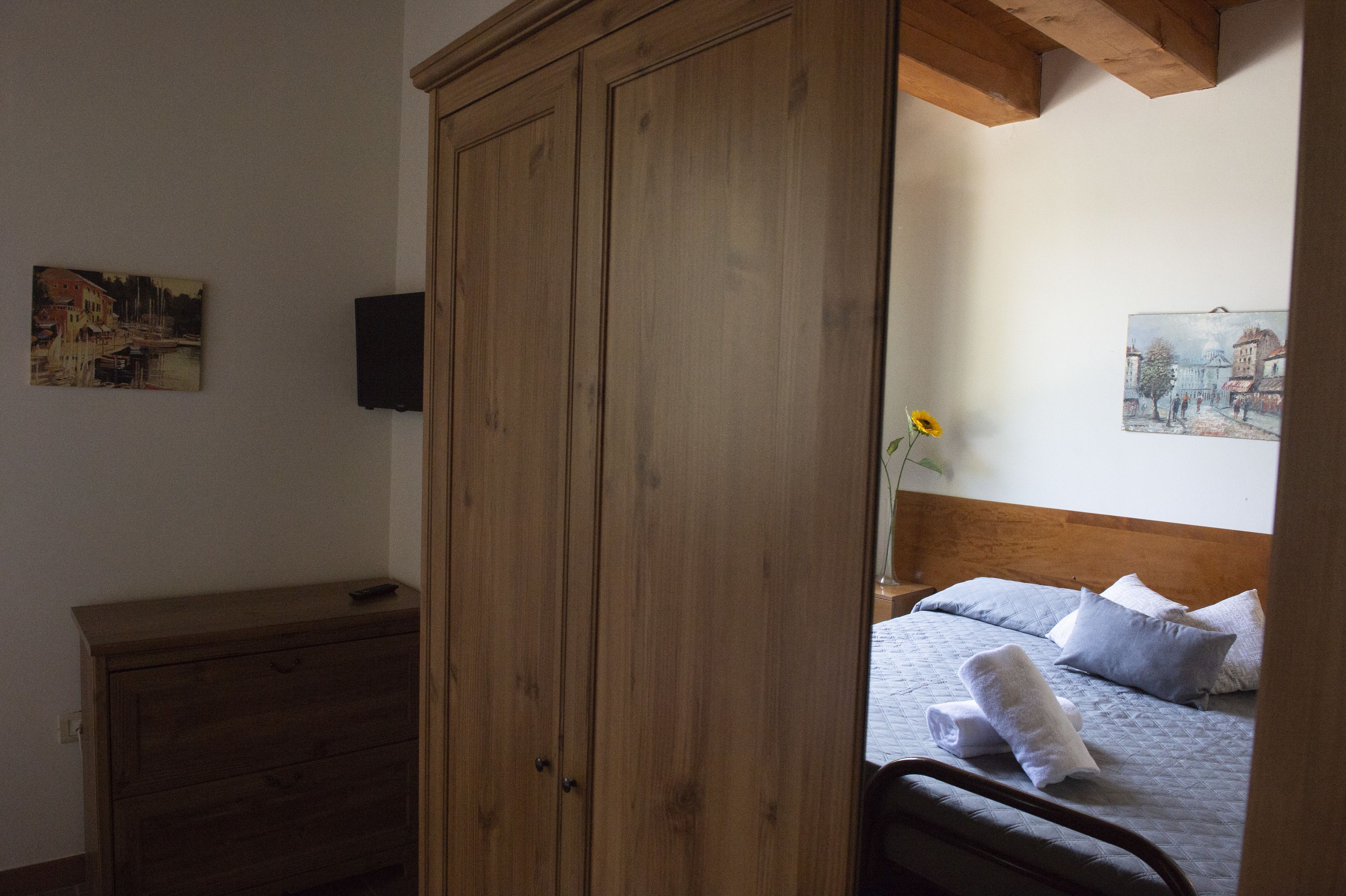 Een slaapkamer met een houten garderobe, een bed met kussens en twee schilderijen aan de wand.