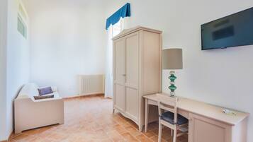 Una habitación con cama, escritorio, armario, radiador y televisor.