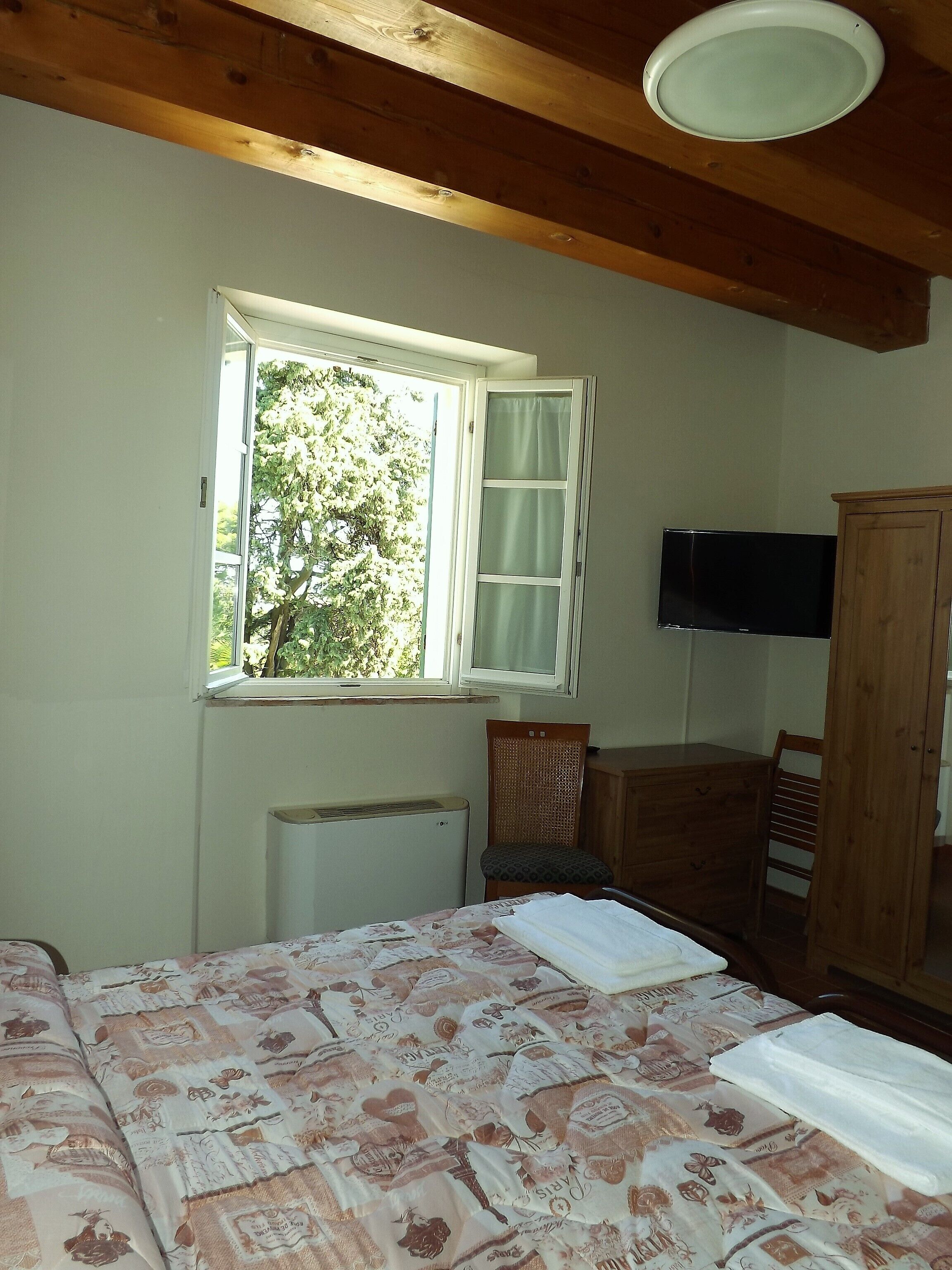 Ein Schlafzimmer mit Bett, Fenster, Heizkörper, Fernseher und Kleiderschrank.