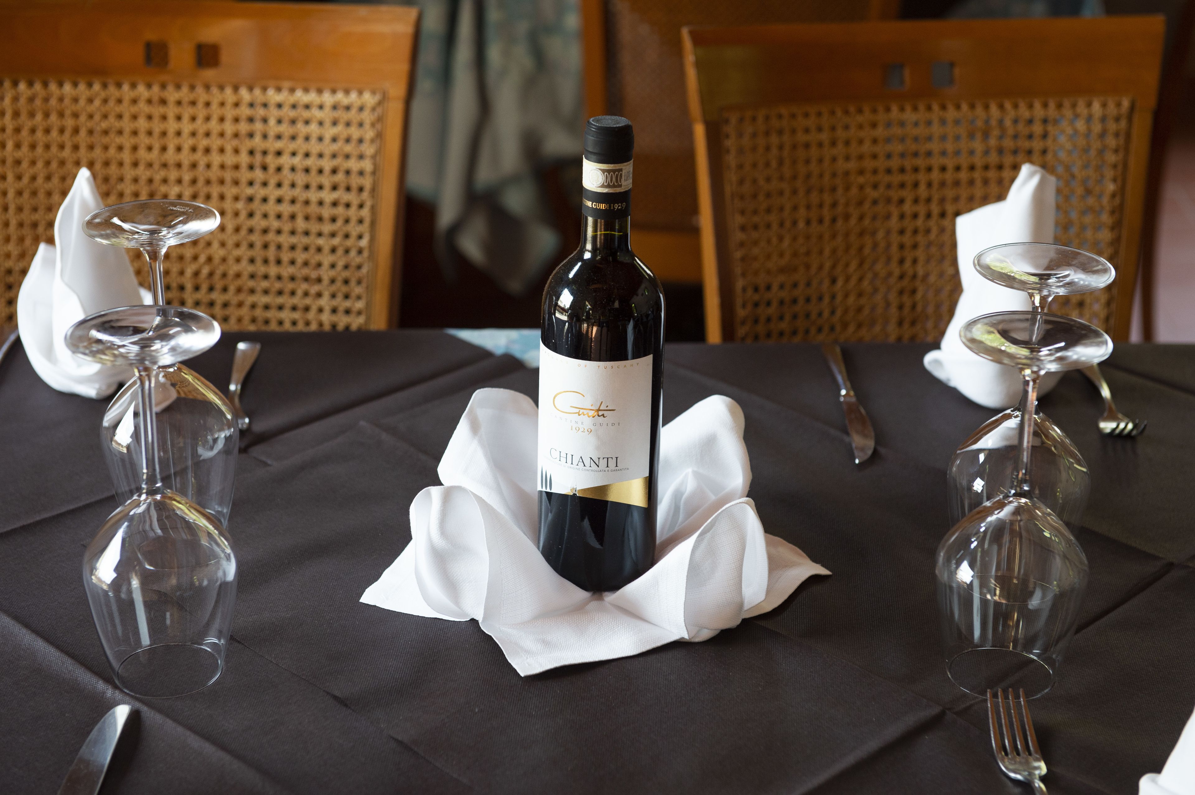 Una mesa preparada para una comida con una botella de Chianti, dos copas de vino y cubiertos.