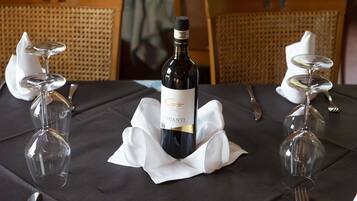 Una mesa preparada para una comida con una botella de Chianti, dos copas de vino y cubiertos.
