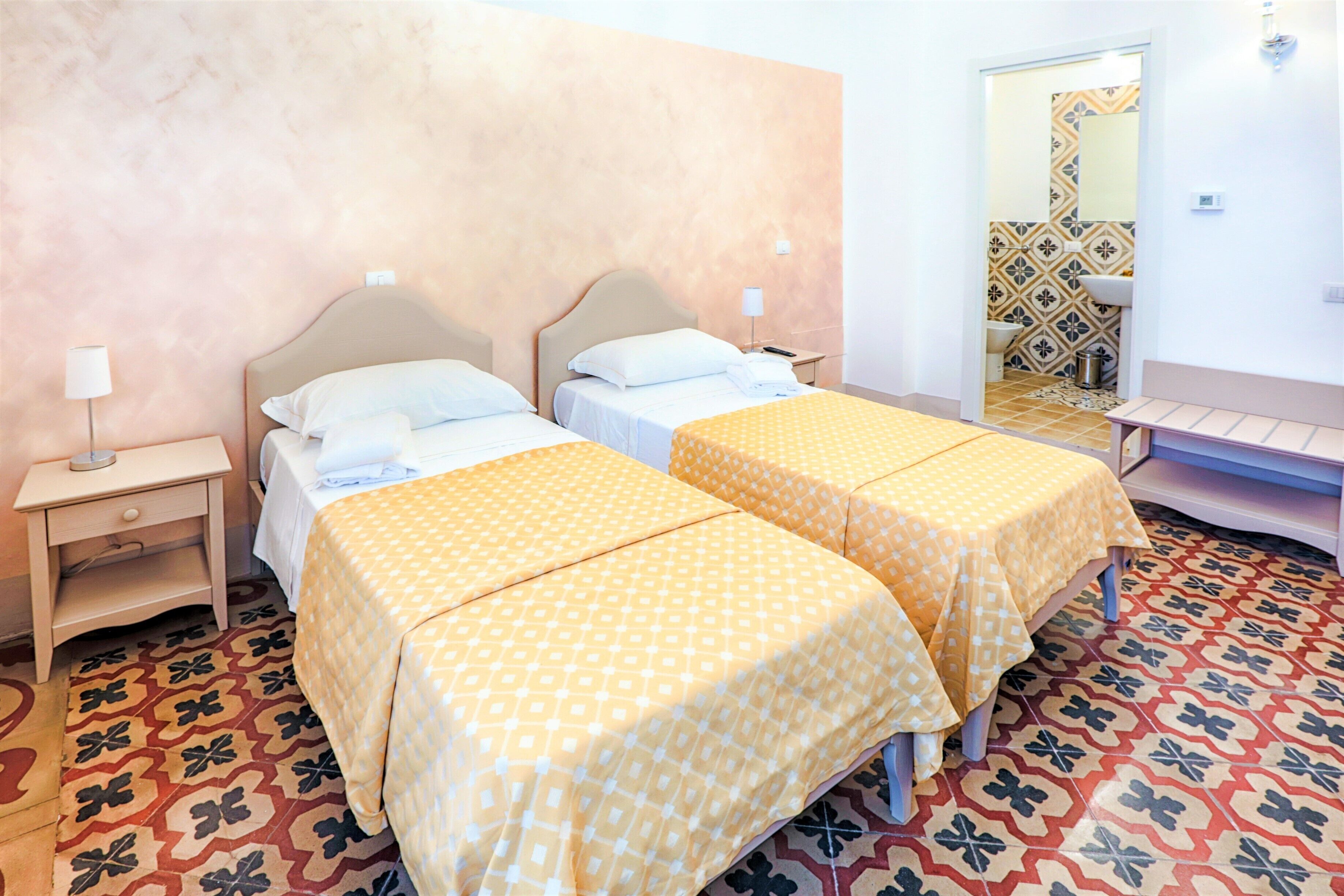 A hotel room with two beds, a nightstand, a lamp, and a bathroom visible through an open door.