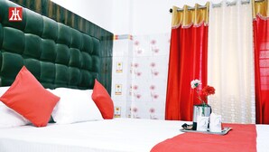 A hotel room with a green upholstered headboard, red and white bedding, and a tray with a vase of flowers. - Hotel Holydon (Siliguri)