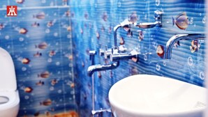 A bathroom with a blue tiled wall, a white sink, and a toilet. - Hotel Holydon (Siliguri)