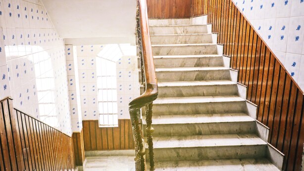 A staircase with wooden handrails and white steps, leading to a landing with a window. - Hotel Holydon (Siliguri)