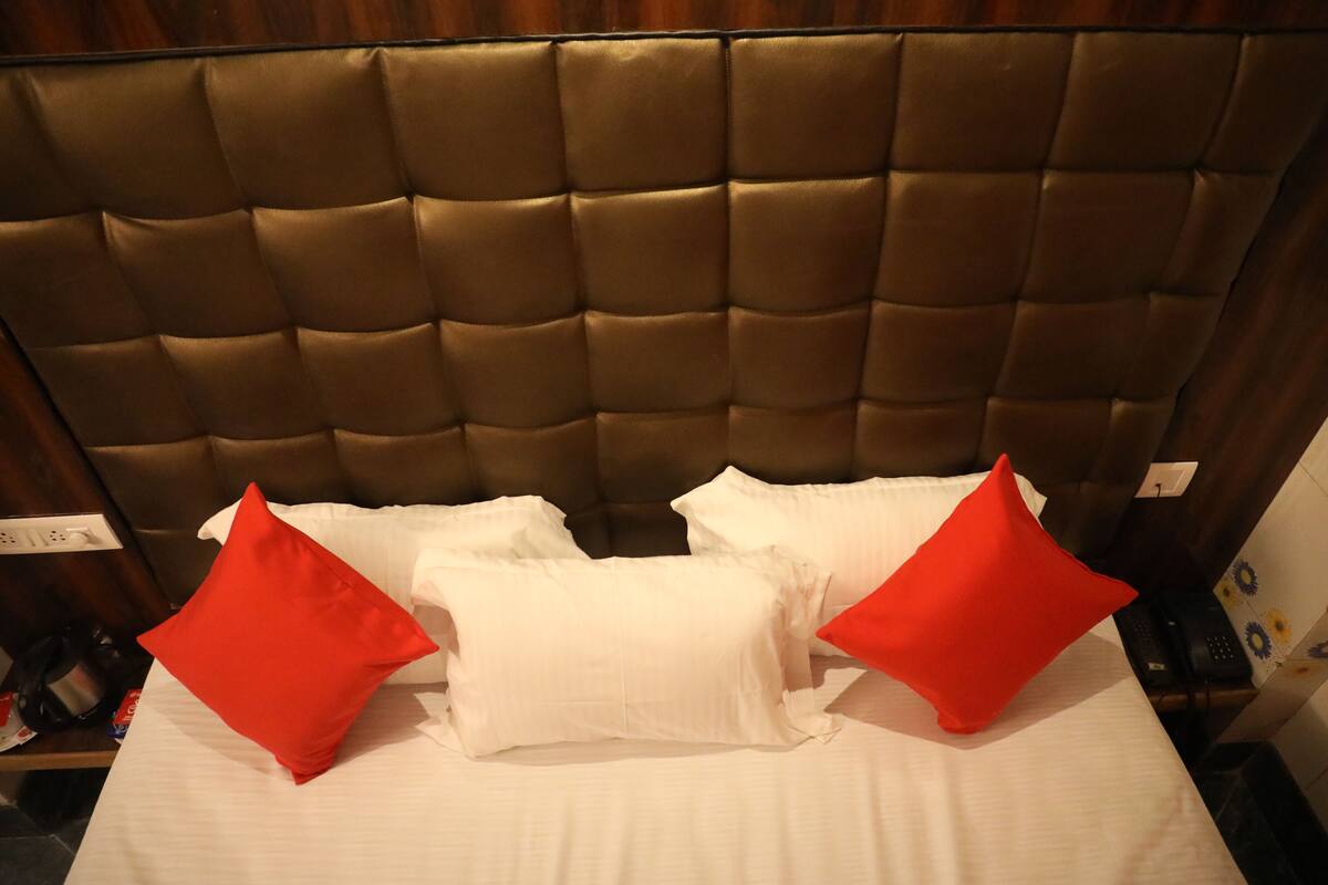 A bed with a tufted headboard, white bedding, and two red pillows.