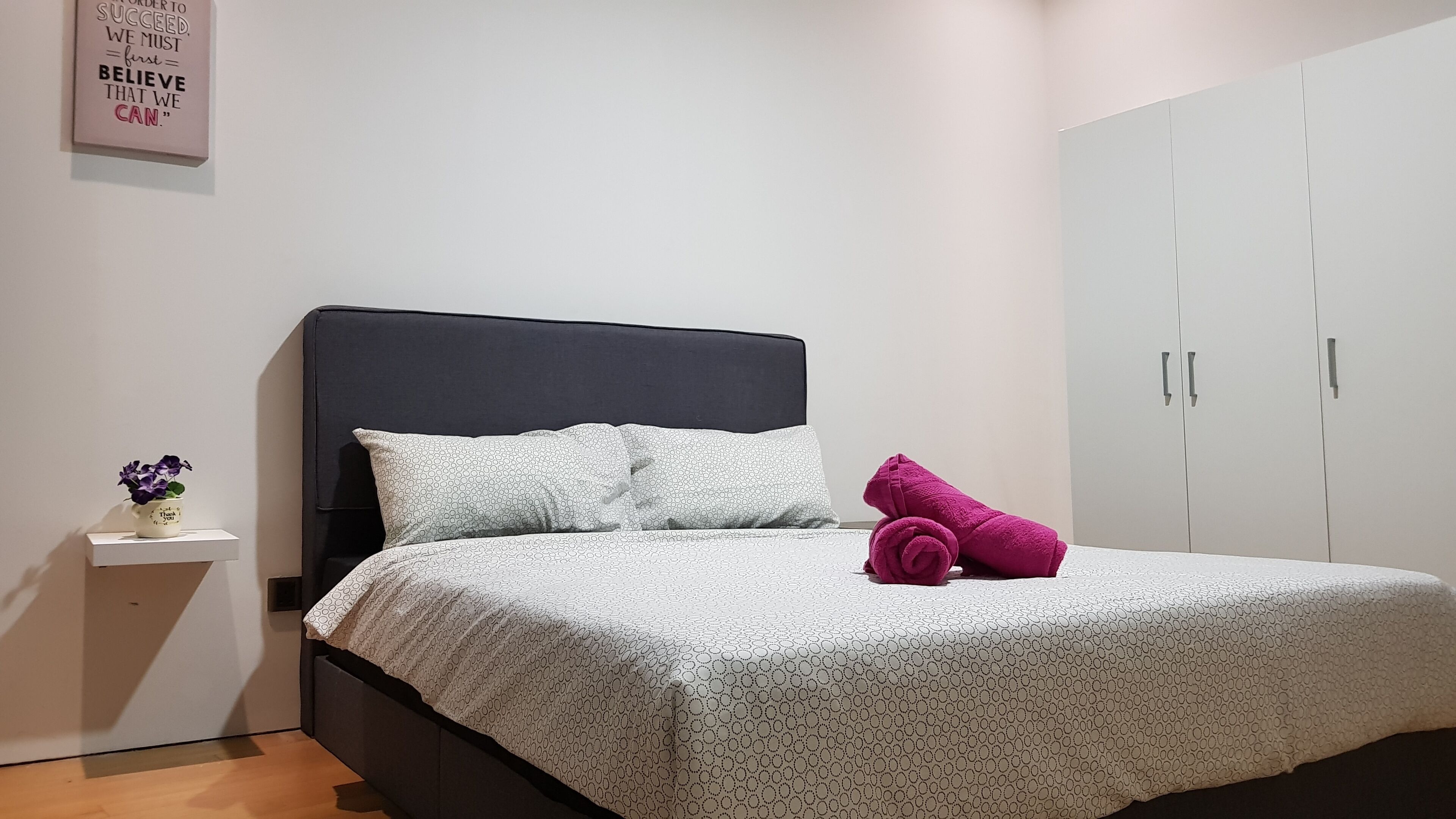 Una cama bien hecha con una colcha estampada, una almohada y una toalla enrollada al lado.