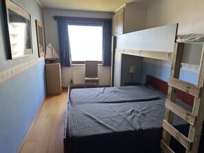 Una habitación pequeña con literas, un escritorio, una silla y una ventana con cortinas.