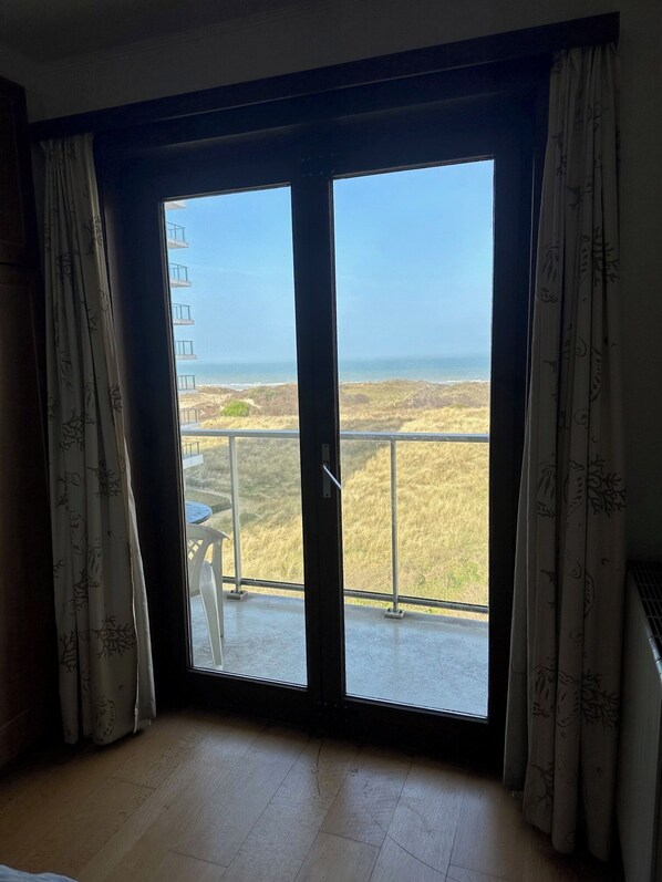 Una habitación con un gran ventanal corredero que da a un balcón con vista al mar y al paisaje distante.