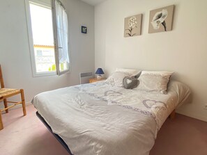 A bedroom with a bed, a chair, a window with curtains, and two wall-mounted pictures.