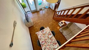 A dining area with a table set for two, a wooden staircase, and a view of the outdoor patio. - Cozy House Near Dunes Beach, 2 Bedrooms + Mezzanine, Parking & Garden, Baby Gear Included (Bretignolles-sur-Mer)