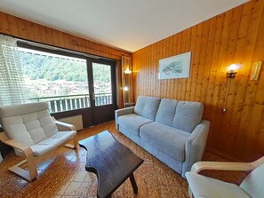 Un'accogliente stanza con parete rivestita in legno, un divano grigio, una poltrona bianca e un tavolino da caffè scuro.