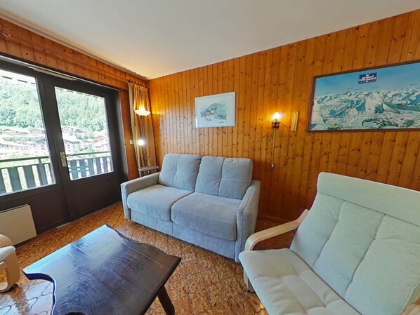 Una stanza con parete rivestita in legno, un divano grigio, una poltrona bianca, un tavolino da caffè in legno scuro e un dipinto con paesaggio montano.