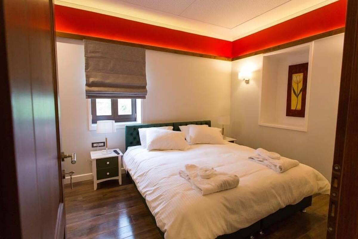 A hotel room with a bed, bedside table, and a window with a blind.