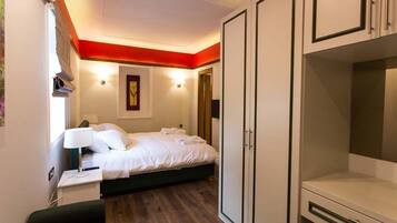 A hotel room with a bed, bedside table, lamp, wardrobe, and a door.