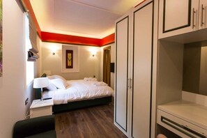 A hotel room with a bed, bedside table, lamp, wardrobe, and a door.