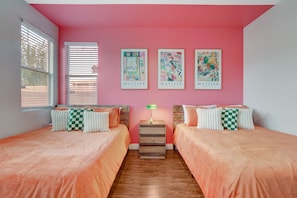 Une chambre avec deux lits, des murs roses et trois tableaux de Matisse.