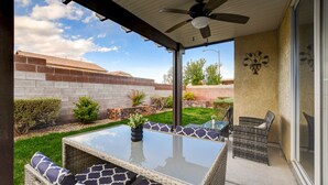 A covered patio with a glass-top table and wicker furniture, a ceiling fan, and a view of a brick wall and greenery. - Near Las Vegas Strip and Airport: Games & Arcades- Southpoint less than 5 mins. (Las Vegas)