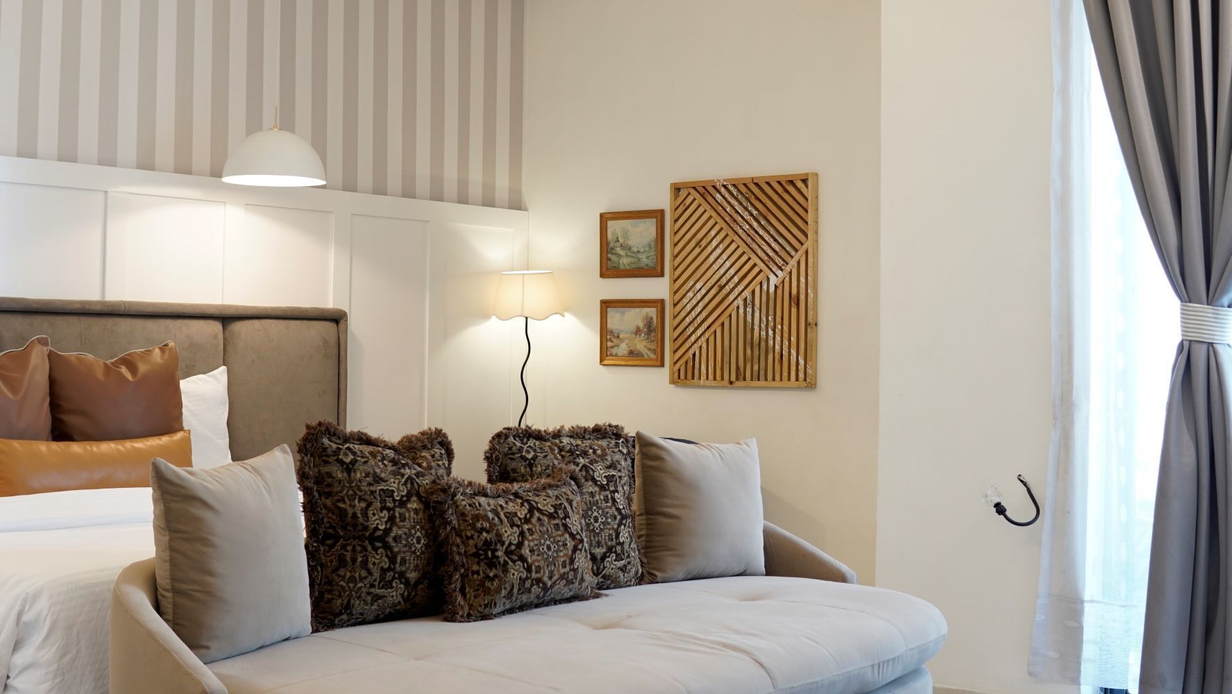 A hotel room with a bed, a sofa, a lamp, and a wall-mounted artwork.