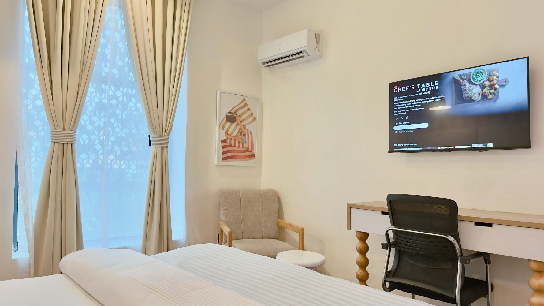 A hotel room with a bed, a chair, a desk, a television, and an air conditioning unit.