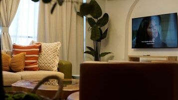 Olohuone, jossa on sohva, koristetyynyjä, televisio ja huonekasvi.