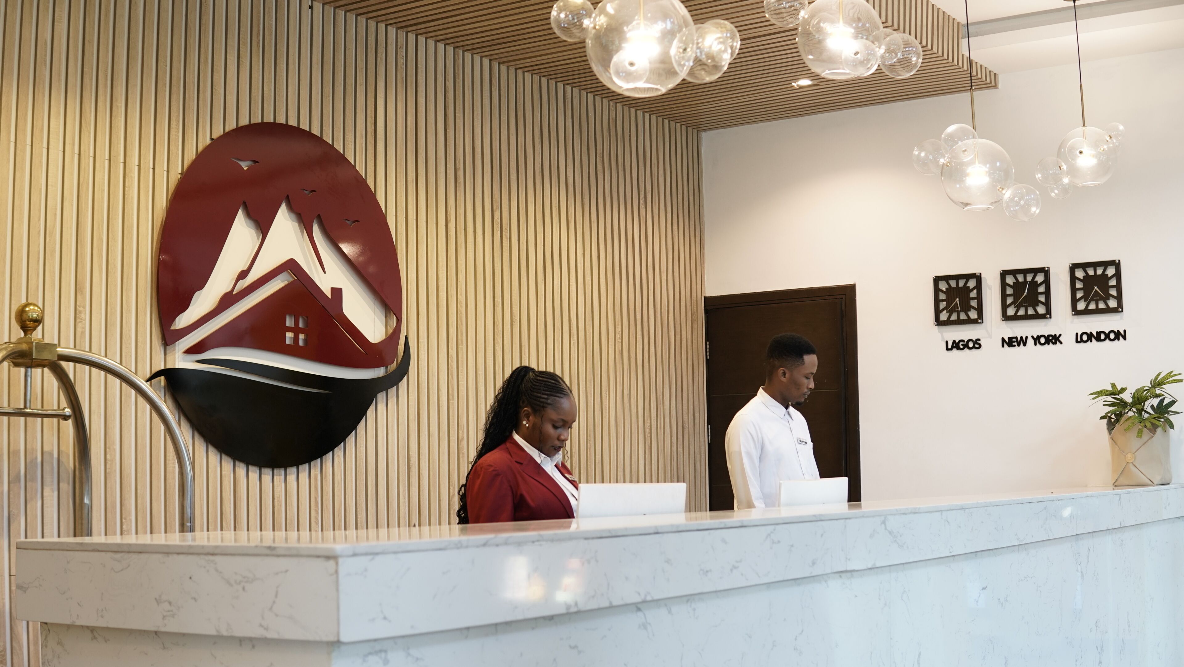 A reception desk with a logo, a wall clock, and a potted plant.