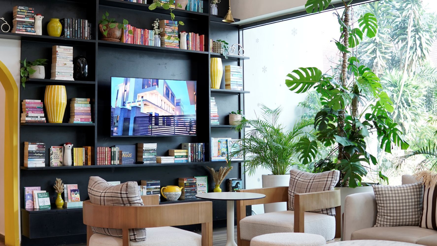 Uma sala de estar com televisão, estantes de livros, uma mesa de centro e uma planta grande.