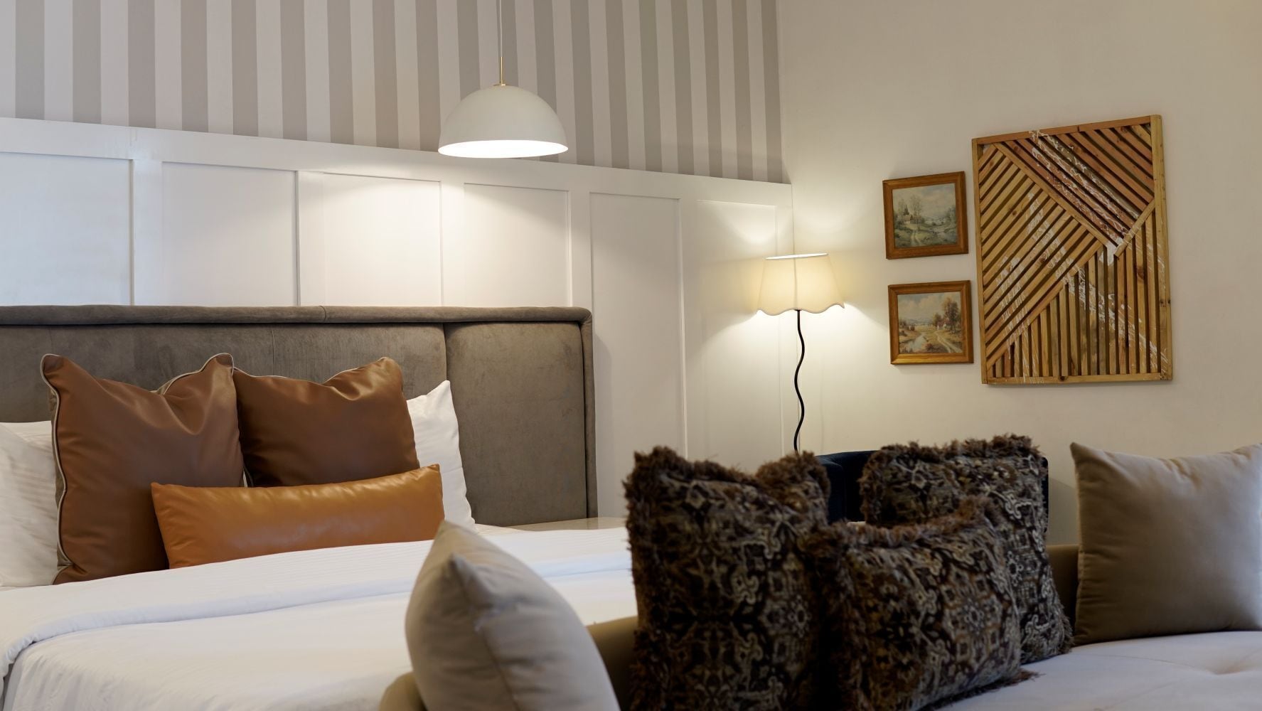 A hotel room with a bed, pillows, a headboard, a wall-mounted lamp, and a decorative panel.