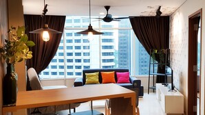 Una sala de estar moderna con una mesa de comedor de madera, sillas negras, un sofá con cojines coloridos y un ventanal con cortinas.