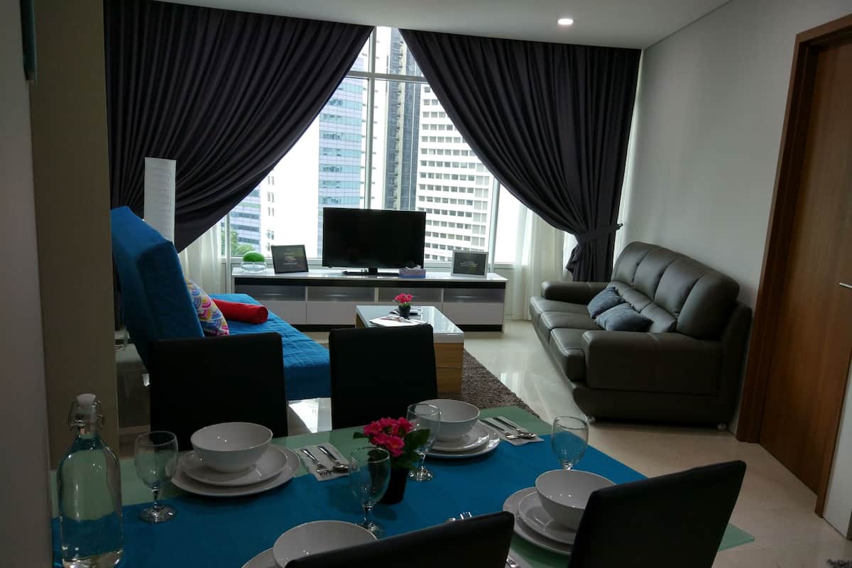 A modern living room with a dining area, a sofa, a television, and a view of a cityscape through large windows.