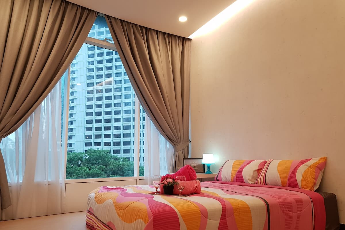 A hotel room with a large bed, a nightstand, a lamp, and a view of a tall building through sheer curtains.